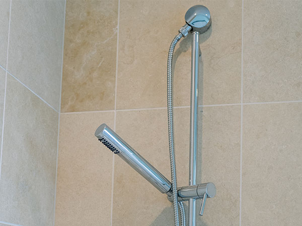 Chrome shower trim, handheld sprayer, and slide bar installed on travertine tile